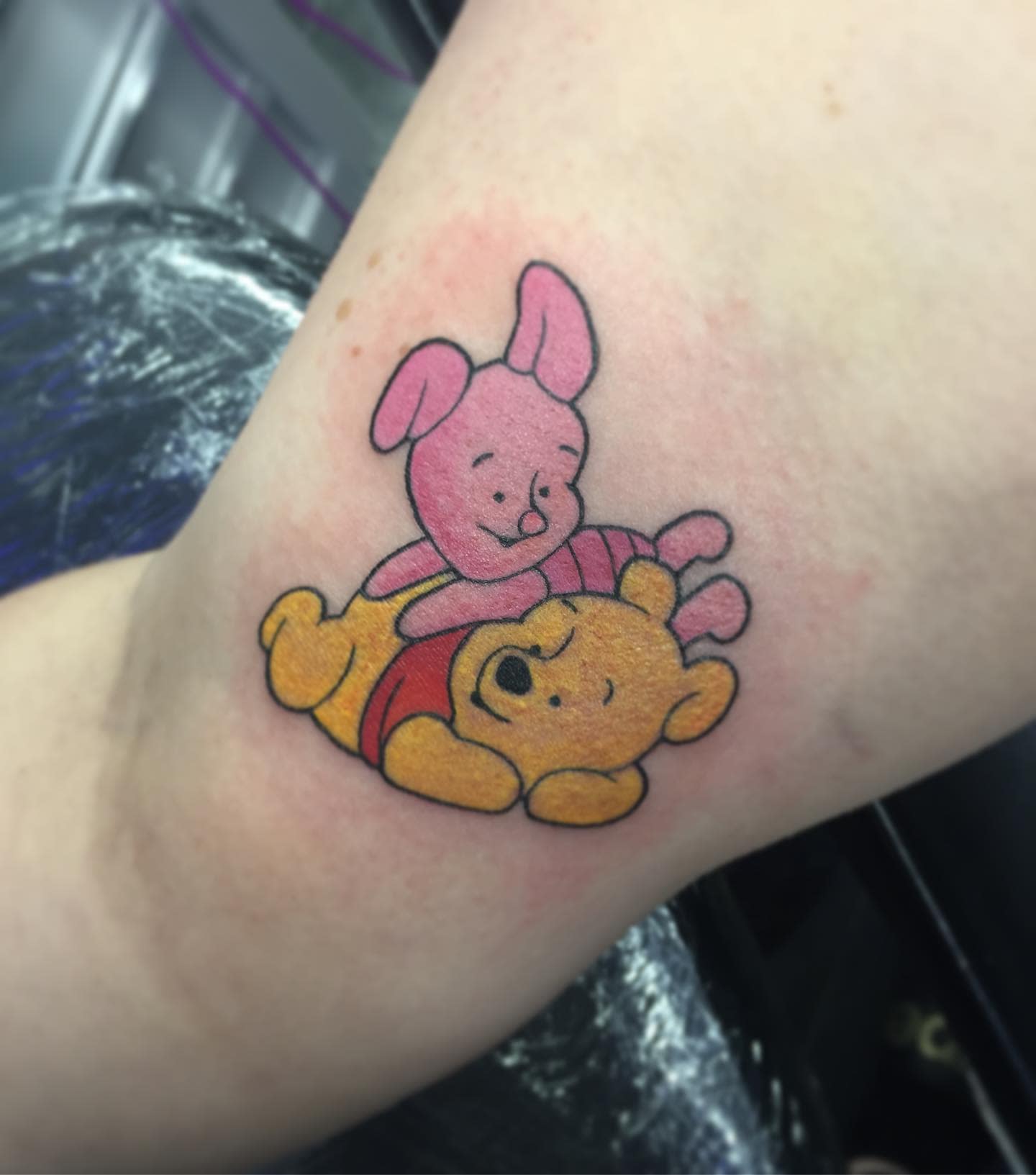 Color tattoo of Piglet hugging a content Winnie the Pooh on a person's arm